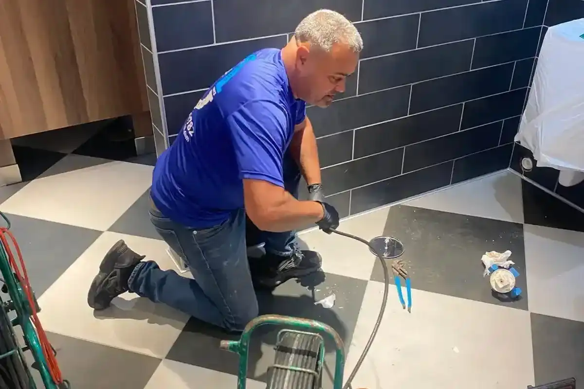 Technician preparing sewer-camera equipment beside an exterior drain access point