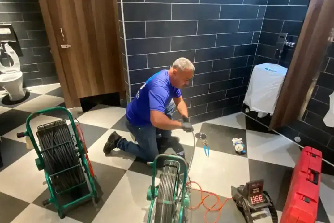 Plumber feeding inspection equipment through a bathroom drain access point