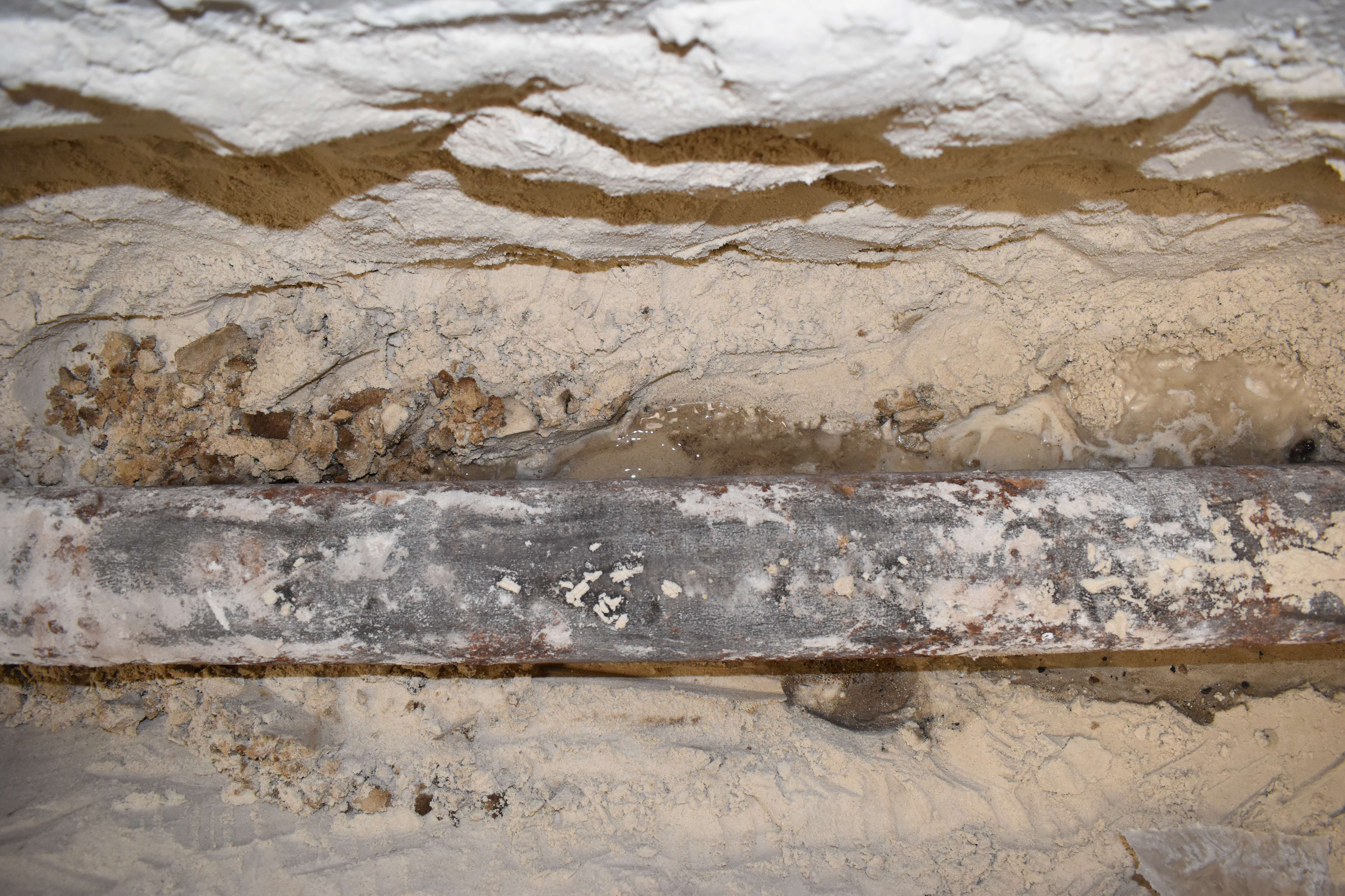 Cast iron pipe exposed behind wall showing water damage and corrosion