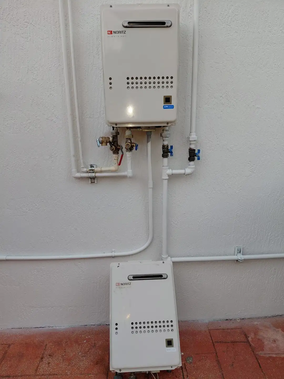 Noritz gas tankless water heaters installed on exterior wall with PVC piping in Miami home