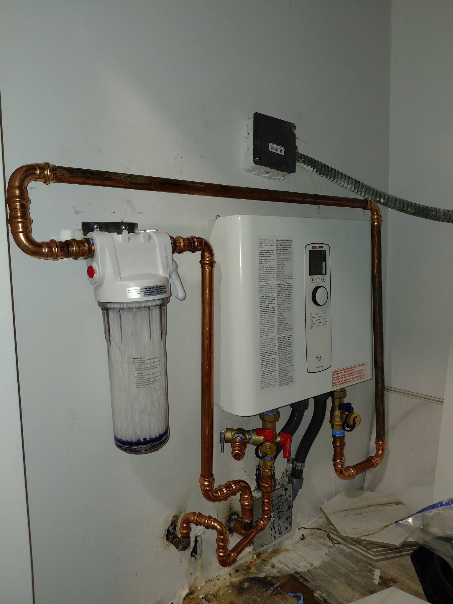 Tankless water heater with inline pre-filter connected via copper piping to protect against hard water