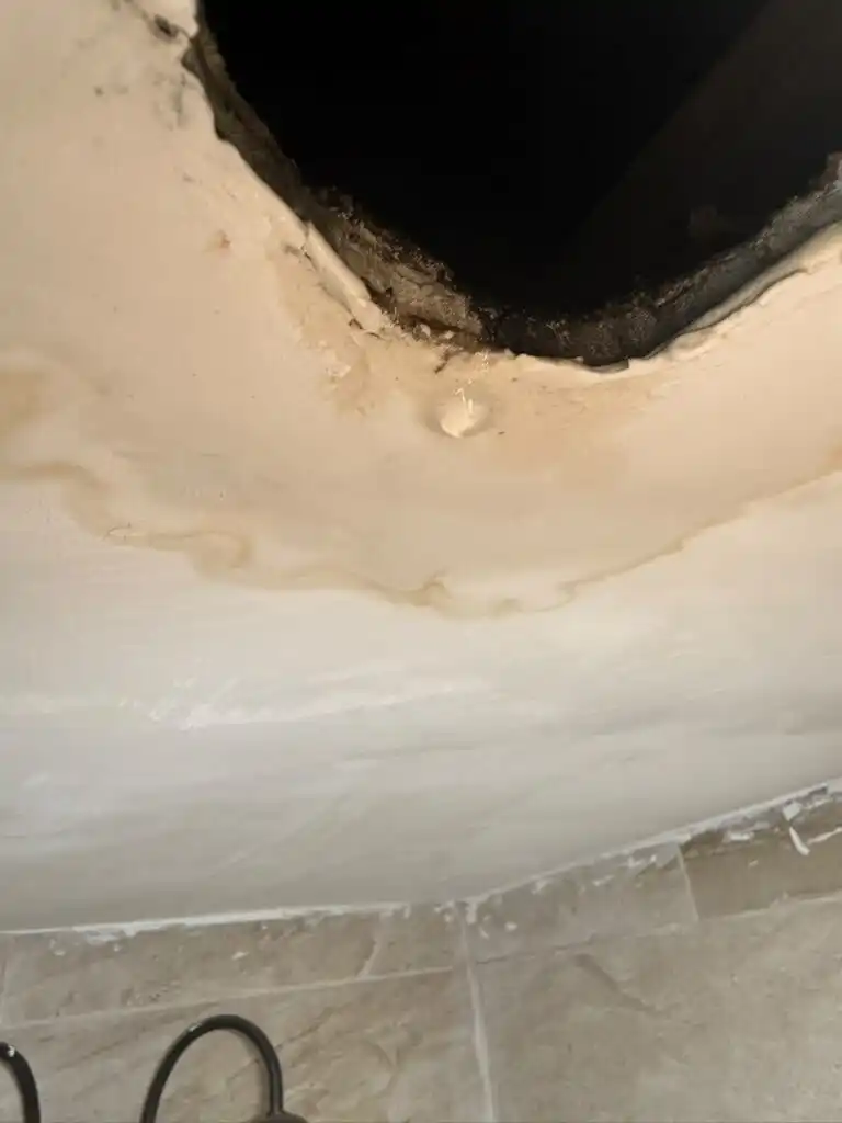 Active ceiling drip over a tiled bathroom from a plumbing leak above.