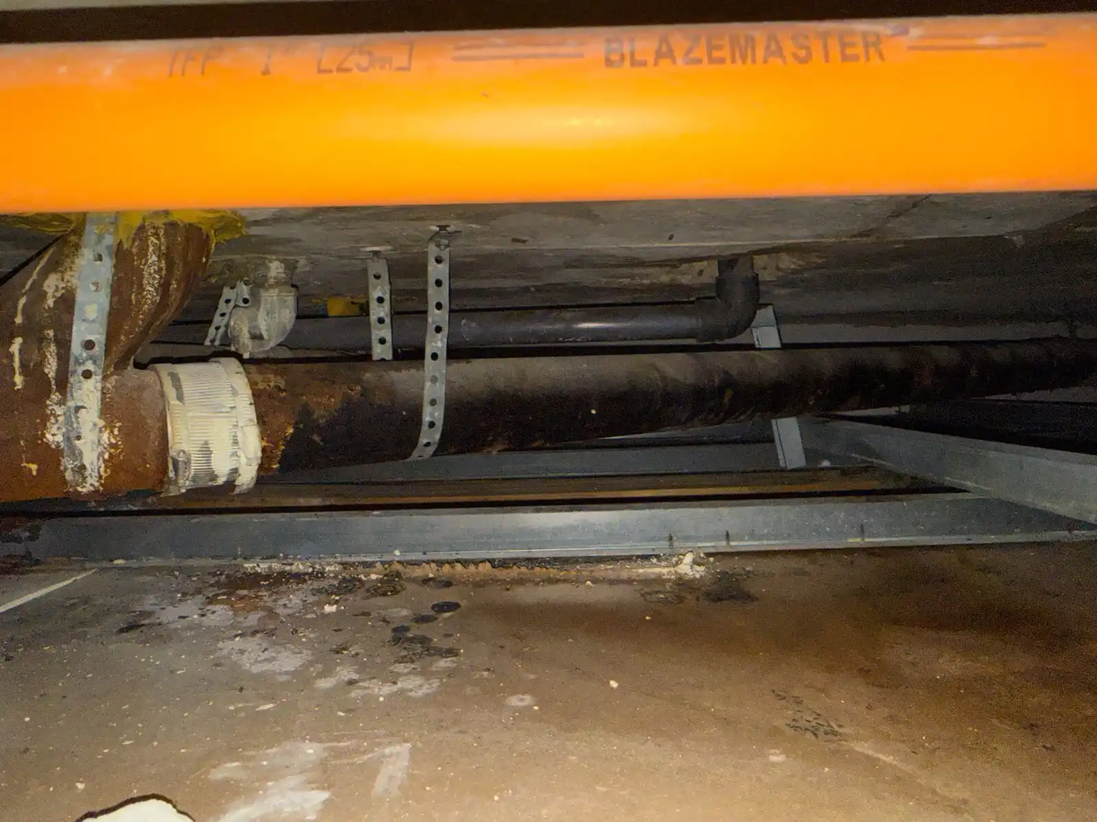 Cast-iron drain with a no-hub coupling in a home crawlspace next to a BlazeMaster sprinkler line.
