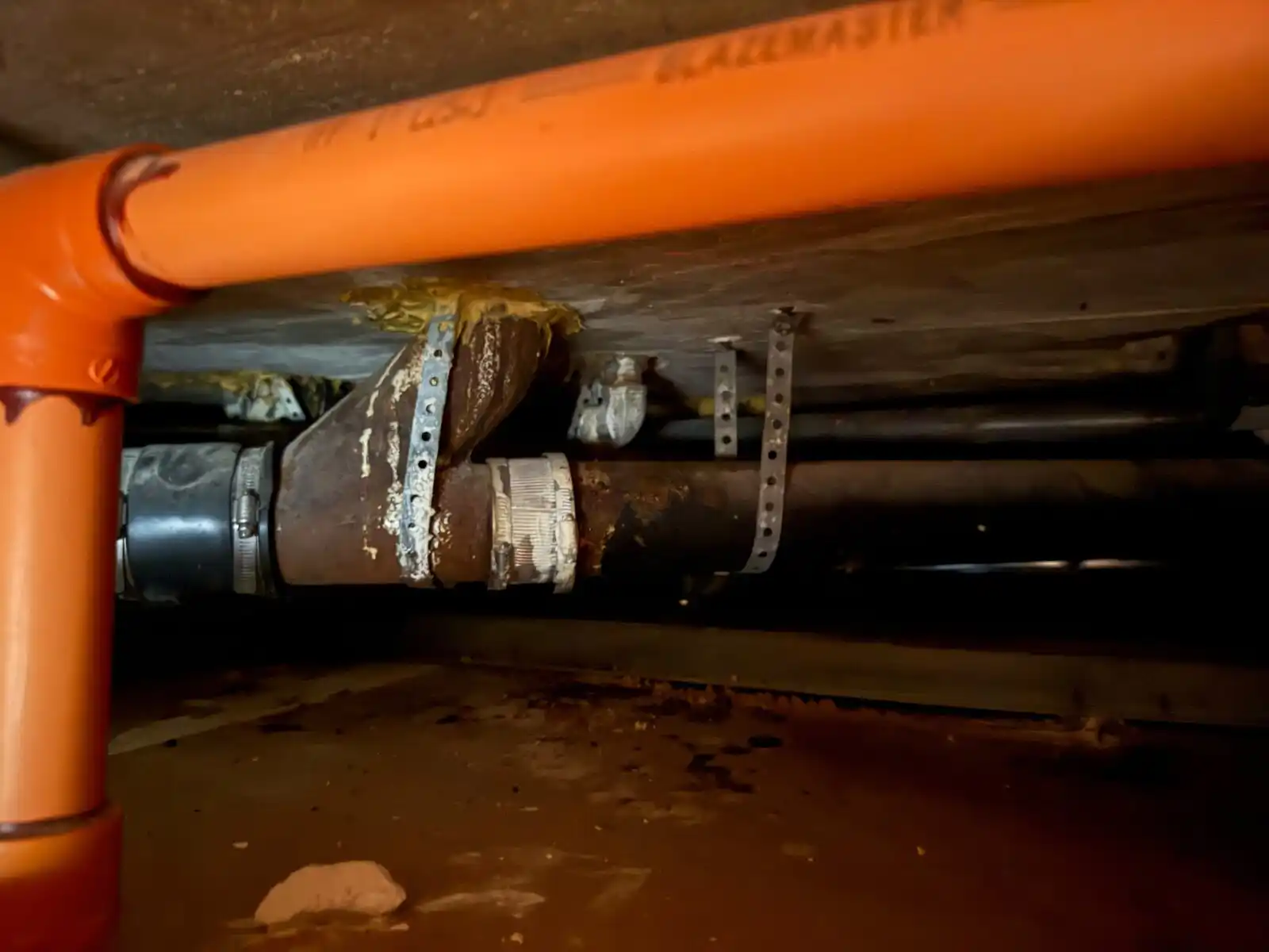 Cast-iron drain wye with no-hub couplings in a crawlspace under a fire sprinkler line.
