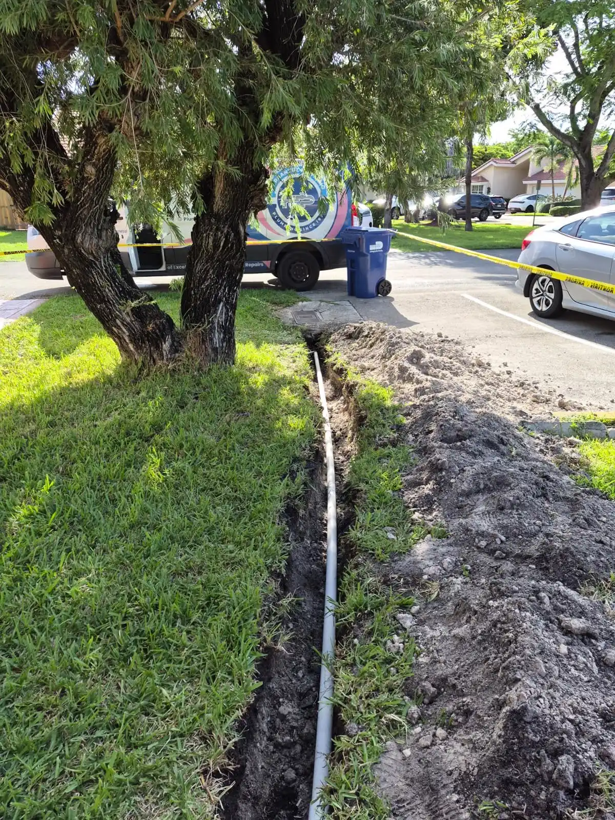 PVC water-line trench in a Hialeah lawn with a plumbing service van on site.