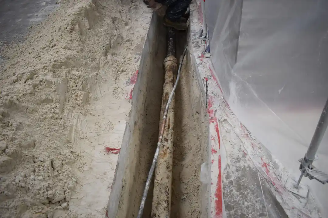 Plumber exposing corroded cast iron pipe in trench for replacement - Hernandez Plumbing